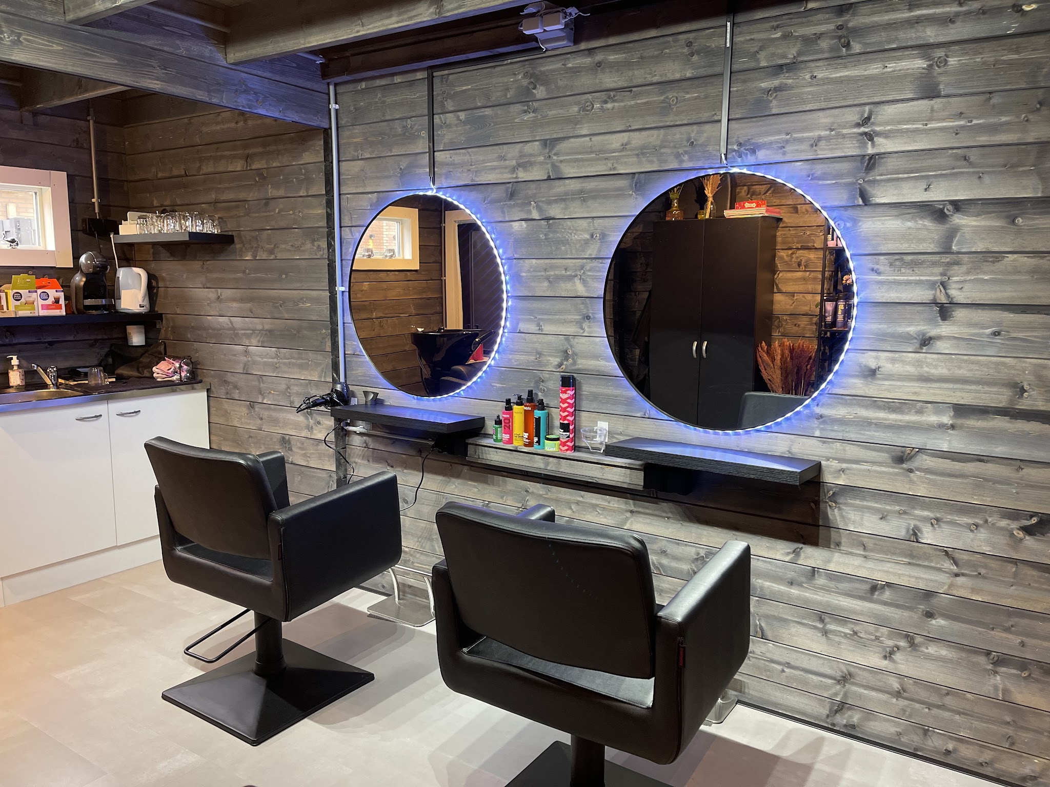 De twee ronde spiegels met blauwe ledrand en de zwarte kappersstoelen in de salon